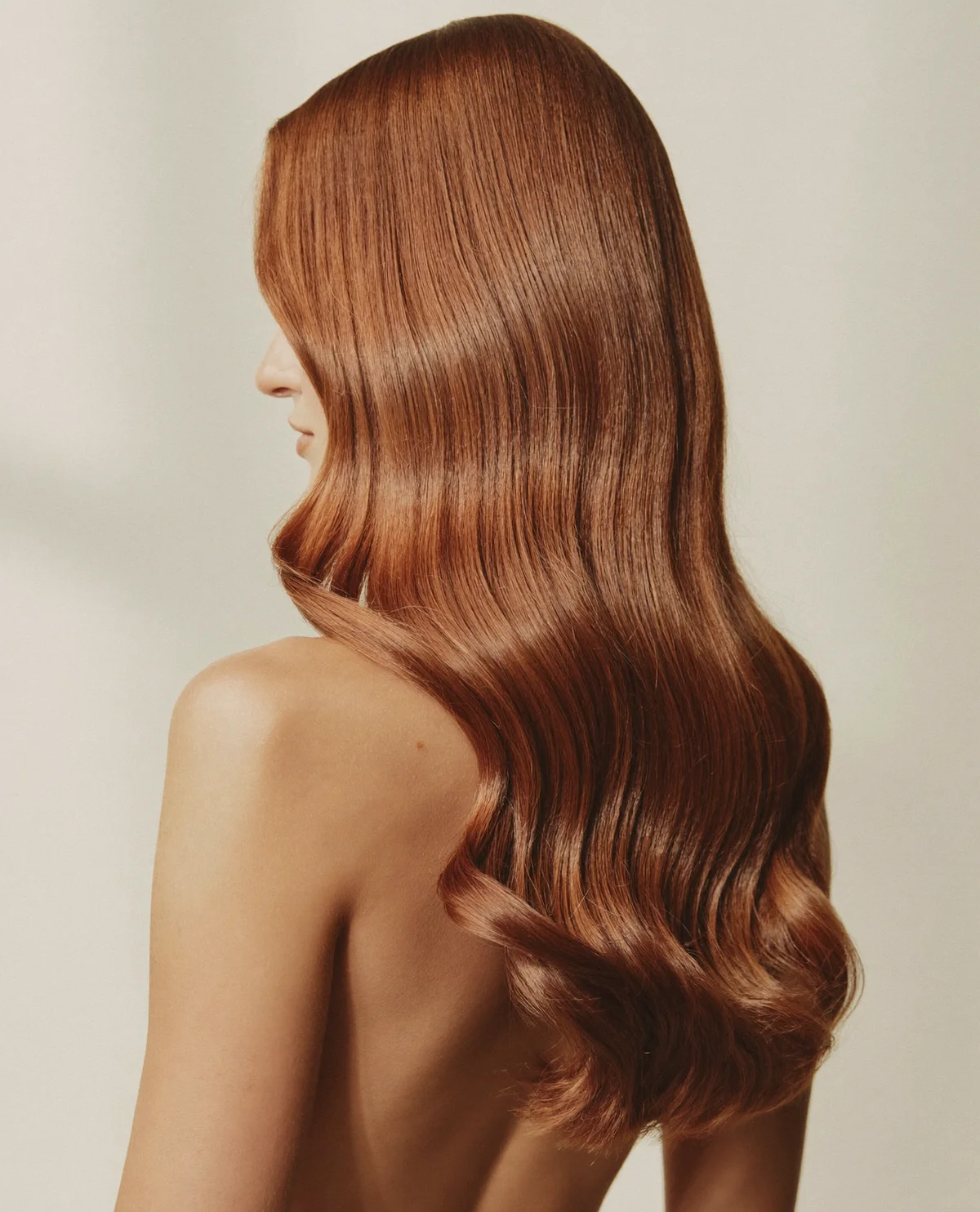 Editorial portrait of glossy copper-toned hair against a cream background